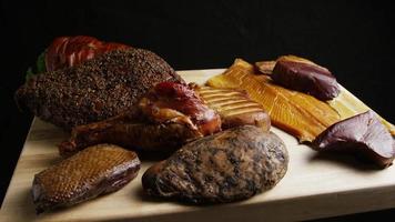 Foto giratoria de una variedad de deliciosas carnes ahumadas premium en una tabla de cortar de madera - comida 052 video