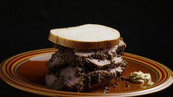 Foto giratoria de un delicioso sándwich de pastrami premium junto a una cucharada de mostaza de Dijon - comida 046 video
