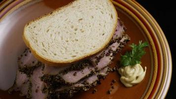 Foto giratoria de un delicioso sándwich de pastrami premium junto a una cucharada de mostaza de Dijon - comida 028