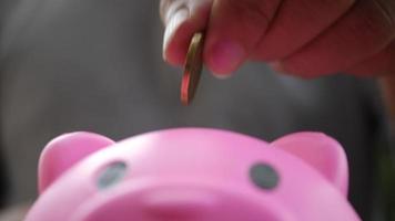 Hand putting coins in a pink piggy bank, saving money concept