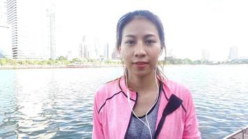 slow motion - asiatisk vacker kvinna i fitnesskläder använder en smartwatch för att lyssna på musik, prata i telefon efter att ha kört i parken. attraktiv hälsosam kvinnlig jogging.