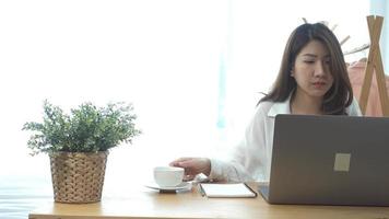 mooie jonge lachende vrouw komt op laptop terwijl u geniet van het drinken van warme koffie zittend in een huiskamer. video