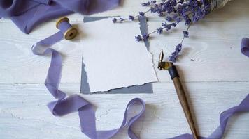 White blank card, envelope and ribbon on a background of pink and blue fabric with lavender flowers on a white background. video