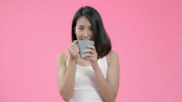 riendo hermosa mujer asiática bebiendo café de té en ropa casual sobre fondo rosa foto de estudio.