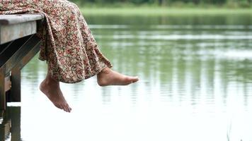 Frau, die ihre Füße am See schwingt und am Rand eines Holzdecks sitzt video