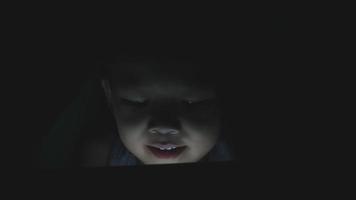 Asian little boy playing tablet or smartphone on a bed in the night video