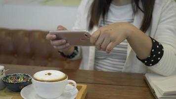 mulher tirando uma foto de seu cappuccino com um smartphone. video