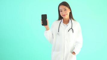 Mulher médica asiática com telefone celular em fundo azul isolado video