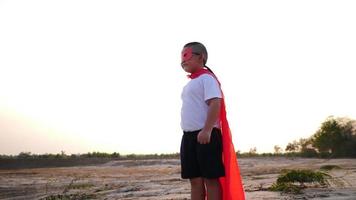 silueta de un niño divirtiéndose vestido como un superhéroe corriendo en un campo video