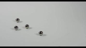 Several little metal balls falling and bouncing on white surface finnaly all balls leave the scene in 4K video