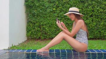 junge asiatische Frau, die am Pool mit ihrem Telefon entspannt video