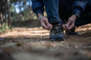Young hiker man ties his shoe laces while backpacking in the forest photo