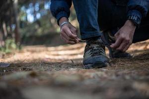 Young hiker man ties his shoe laces while backpacking in the forest photo