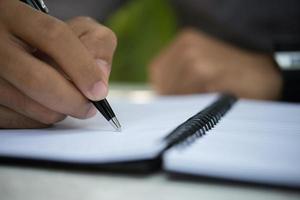 Hombre escribiendo en el bloc de notas mientras está sentado relajándose en el jardín de su casa foto