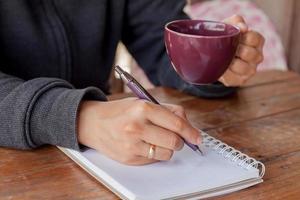 Person holding a coffee cup and writing in a notebook photo