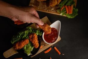 Hand dipping crispy fried chicken into sauce photo