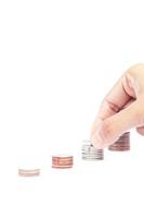 Hand placing a coin on a stack on a white background photo