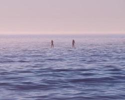 Dos personas de pie sobre tablas de surf en el mar al amanecer. foto