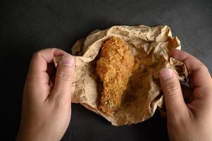 Hands picking up crispy fried chicken on brown paper photo