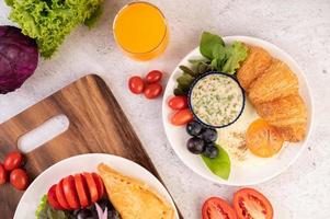 croissant, huevo frito, aderezo para ensaladas, uvas negras y tomates foto