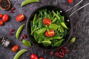 Stir-fried kale in a pan with tomatoes and peppers, top view photo