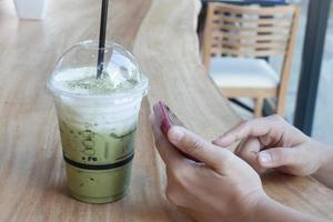 Person holding a phone with an iced green tea photo