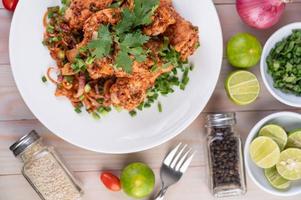 Spicy minced chicken on a plate with cucumber, lettuce and side dishes on wooden table photo