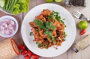 Spicy minced chicken on a plate with cucumber, lettuce and side dishes on wooden table photo