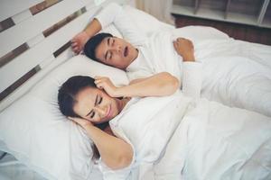 Sleeping woman blocking ears with man snoring in bed photo
