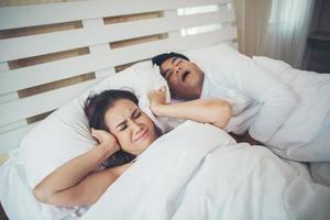 Sleeping woman blocking ears with man snoring in bed photo