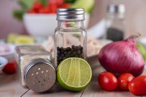 Sliced lime with two shakers and other vegetables on a wooden table photo