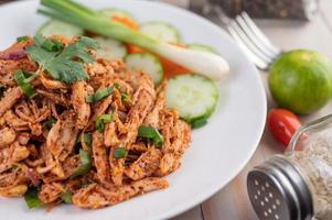 Spicy minced chicken on a plate with cucumber, lettuce and side dishes on wooden table photo