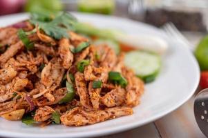 Spicy minced chicken on a plate with cucumber, lettuce and side dishes on wooden table photo