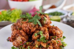 Spicy minced chicken on a plate with cucumber, lettuce and side dishes on wooden table photo