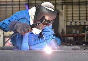 Welder in blue uniform welding the workpiece photo