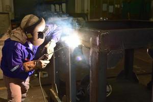 Welder in blue uniform welding the workpiece