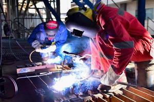 Soldador en uniforme rojo soldando la pieza de trabajo foto