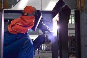 Welder in blue uniform welding the workpiece photo