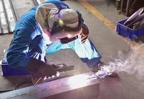 Welder in blue uniform welding the workpiece