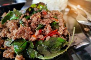 Saltee la carne picada frita con chile y albahaca y arroz al vapor sobre placa negra foto