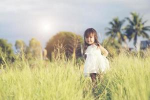 Happy little girl standing in the meadow in a white dress photo