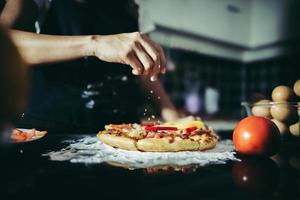 Close-up de una mano poniendo orégano sobre una pizza foto