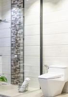Baño amplio y moderno con azulejos brillantes con ducha de vidrio, inodoro y lavabo. vista lateral foto