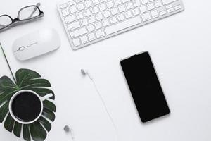 Minimal Office desk table top view with Smart phone, Earphones, Keyboard computer, mouse, Glasses,  coffee cup on a white table with copy space, White color workplace composition, flat lay photo