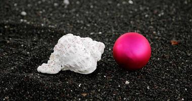 adorno navideño y una concha de mar con gotas de agua sobre la arena negra foto