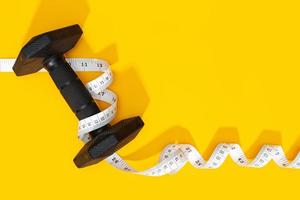 Dumbbells and measure tape on yellow background photo