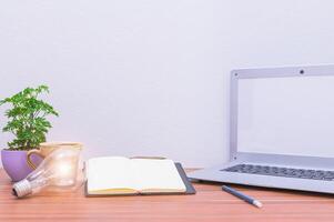Laptop on wooden desk with notebook, plant and lamp photo