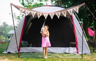 Little Asian girl standing in front of tent while going camping photo