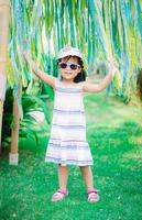 Retrato de linda niña asiática llevar gafas de sol y sombrero en el parque foto