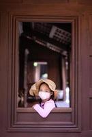 Niña asiática con una máscara contra la contaminación del aire cuando abre la ventana foto